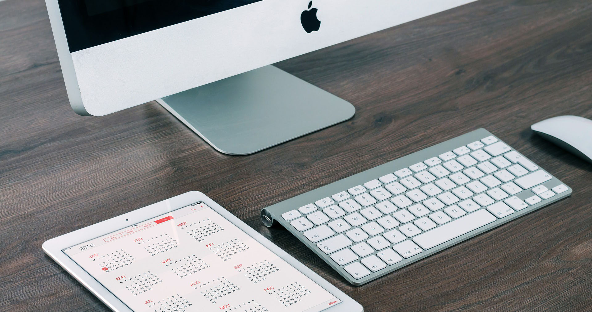 Computerbildschirm, neben dem ein Tablet mit geöffneten Kalender liegt
