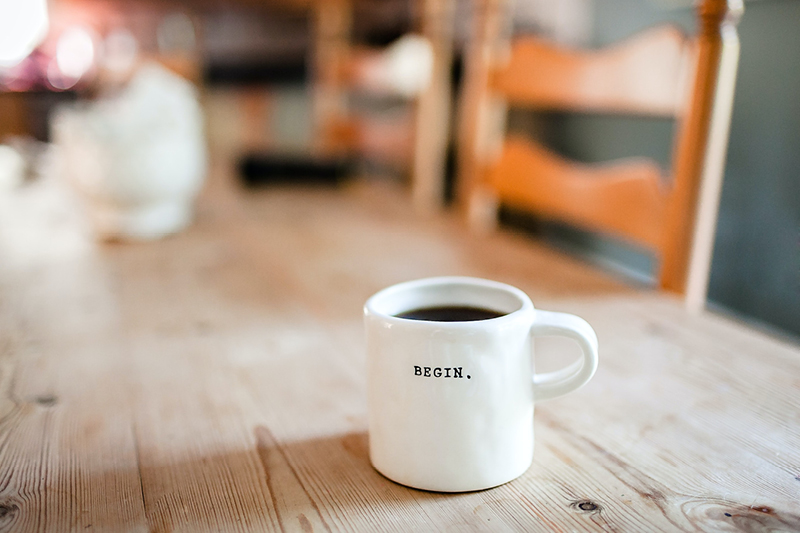 Kaffeetasse mit der Aufschrift Begin., welche mitten auf einem Esstisch steht