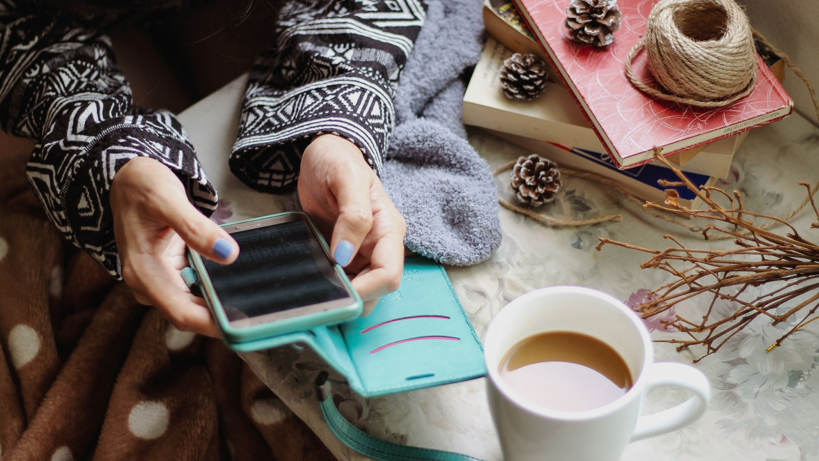 Frau sitzt an einem weihnachtlich geschmückten Tisch und schaut in ihr Handy