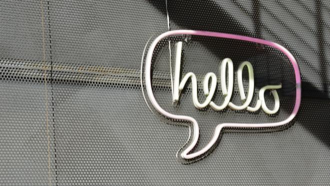 Leuchtsprechblase mit der Aufschrift "hello" vor einem schwarzen Gitter
