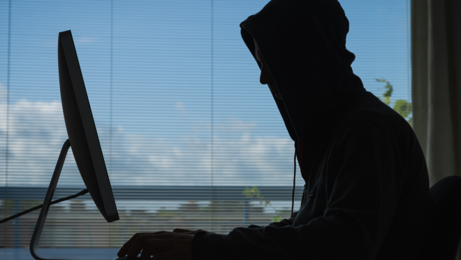 Schatten eines Mannes mit Kapuze der vor einem Laptop sitzt 