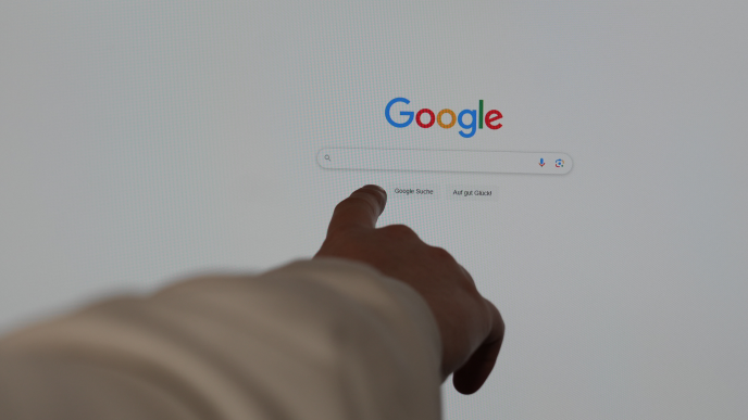Finger zeigt auf die Google-Suchleiste auf einem Computerbildschirm.