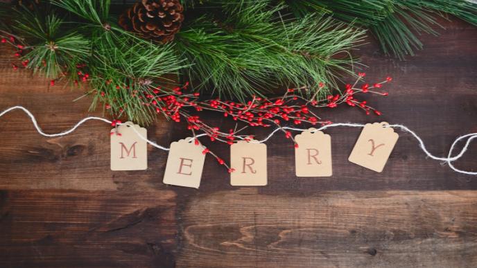 Fünf Holzscheiben, die das Wort "Merry" bilden mit weihnachtlichen Zweigen als Deko