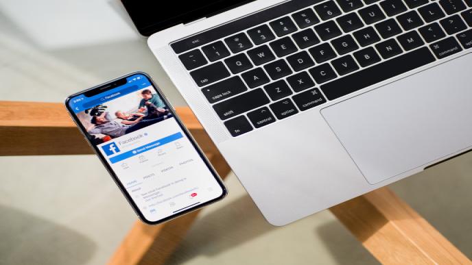 Ein Handy mit geöffneter Facebook App, das neben einem Laptop liegt