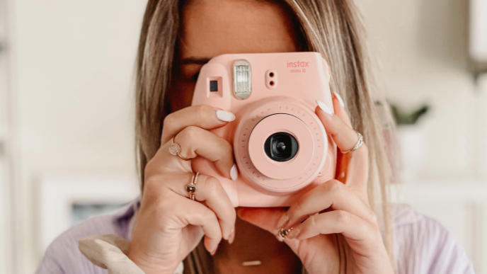 Frau die eine rosane Instax Kamera in den Händen vor ihr Gesicht hält