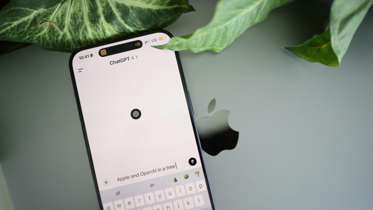 martphone mit geöffneter ChatGPT-App auf einem MacBook neben grünen Blättern.