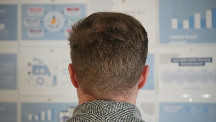 Mann von hinten betrachtet eine Wand mit Diagrammen.
